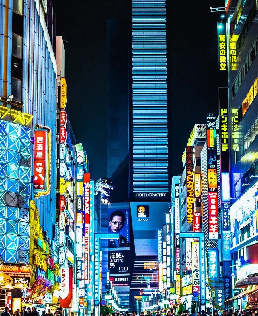 A wide-angle night street scene in Tokyo, glowing neon signage and crowds beneath towering illuminated signboards.