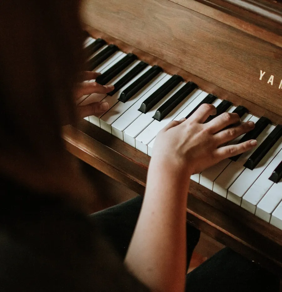 An intimate close-up of hands resting on vintage piano keys, captured in soft low light with charcoal and ivory tones.